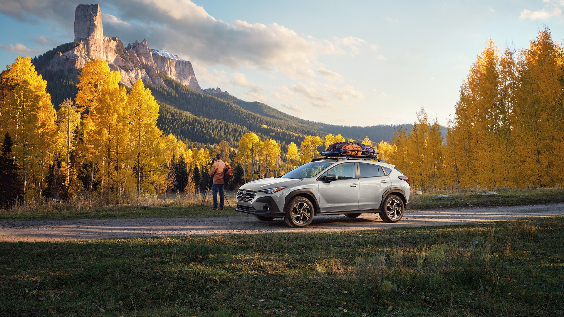 Silver Subaru SUV parked on a dirt road surrounded by bright yellow fall trees and mountains.