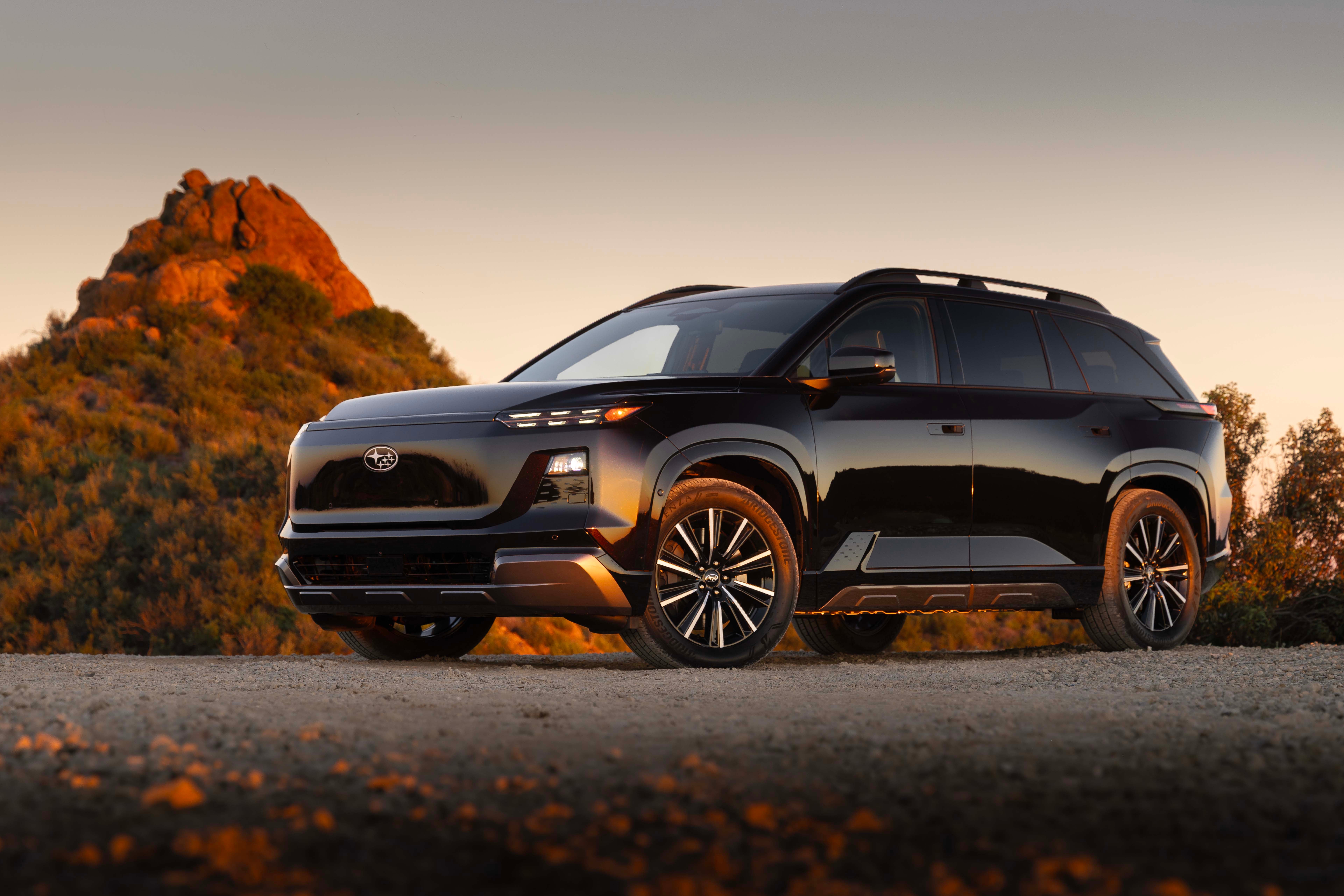 Black Subaru Solterra electric SUV on a dirt road with desert rock formation in the background.