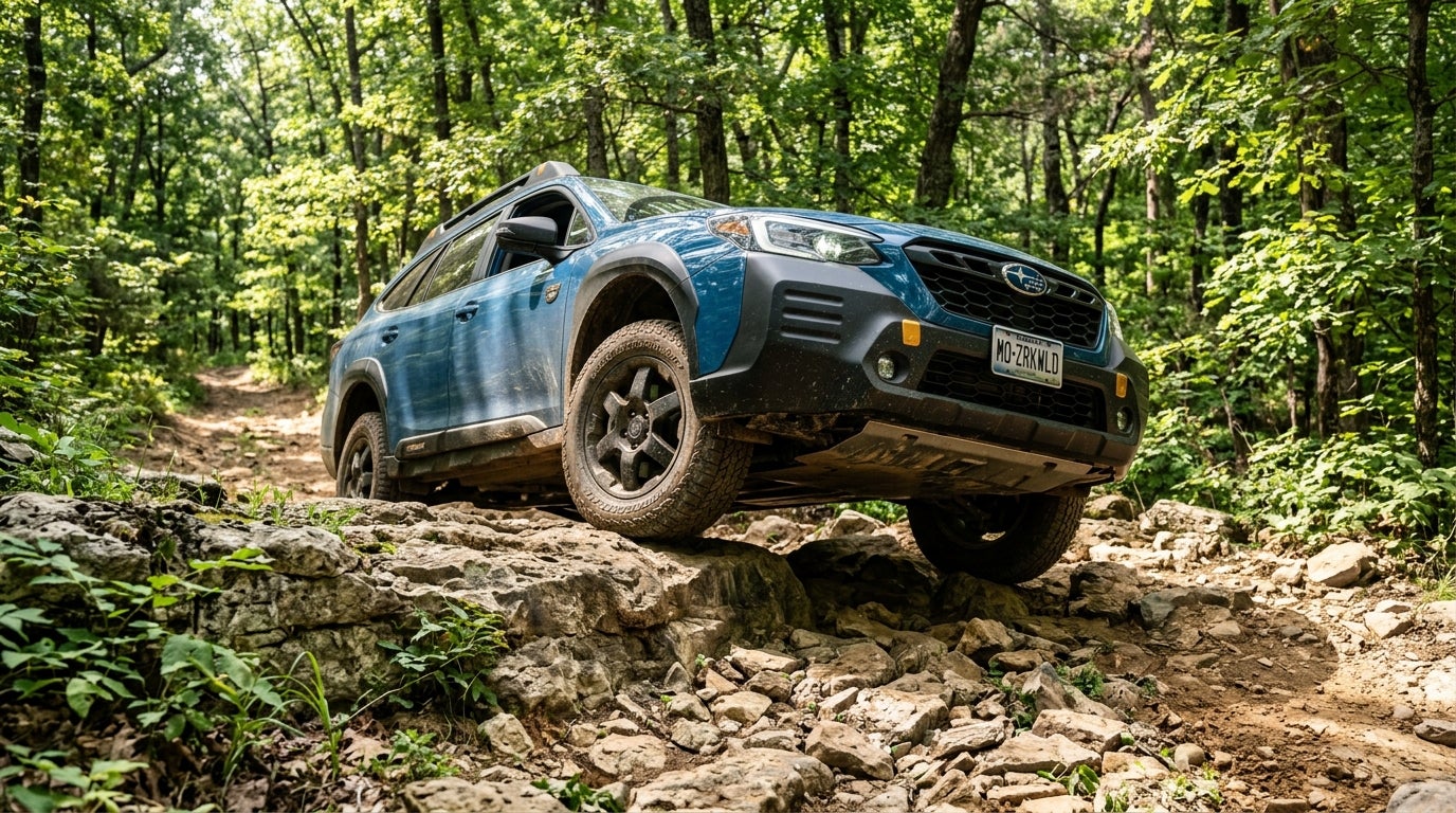 AI generated: A 2026 Subaru Outback Wilderness in Geyser Blue navigating a rugged, rocky trail deep within the Missouri Ozarks, low-angle perspective emphasizing the impressive ground clearance as the vehicle crawls over textured limestone ledges and jagged rocks, dense forest canopy of oak and hickory trees in the background, dappled sunlight filtering through summer leaves, bright afternoon atmosphere, dusty trail with hints of Missouri red clay, cinematic composition, sharp focus on the rugged all-terrain tires and protective undercarriage, no people, realistic textures, natural color palette with rich forest greens and earthy grays, professional outdoor adventure photography style, high-resolution detail.