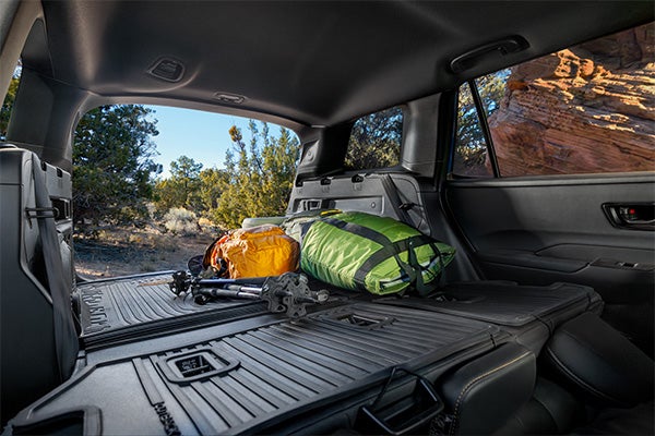 Interior view of an SUV cargo space packed with camping gear and trekking poles looking out an open hatch.