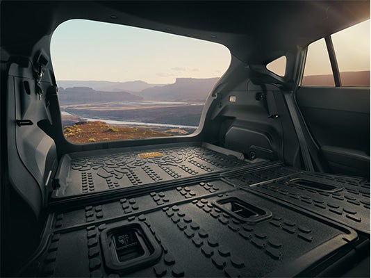 Looking out from the open rear cargo area of an SUV with folded seats toward a scenic canyon landscape at sunset.
