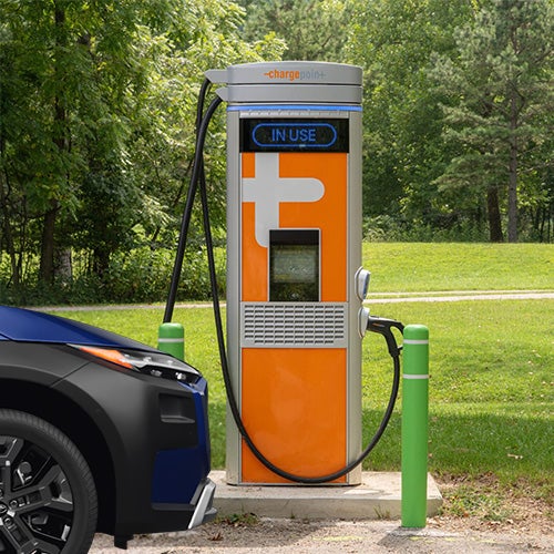 Electric vehicle charging at a ChargePoint station in a park setting.