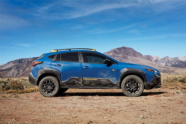 Blue Subaru Crosstrek Wilderness parked on a dirt trail with mountains in the background.