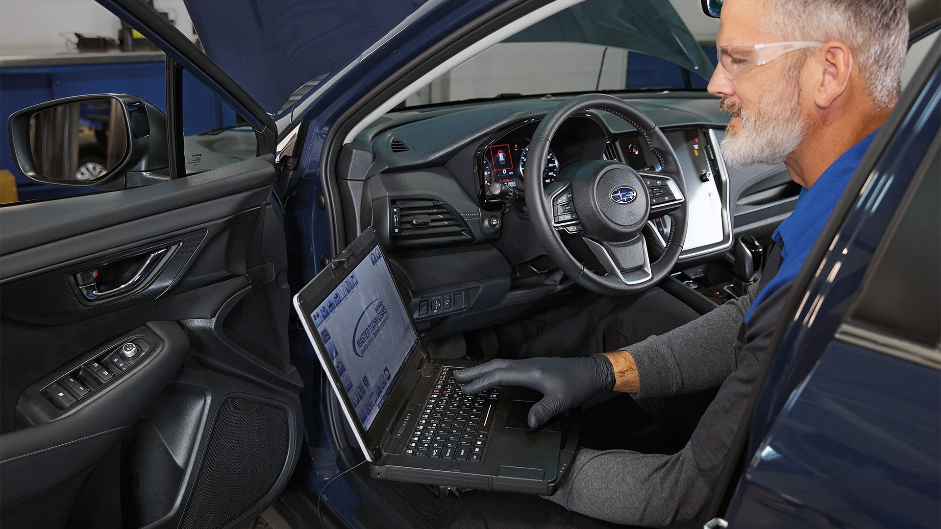 Technician using laptop to diagnose Subaru inside vehicle.