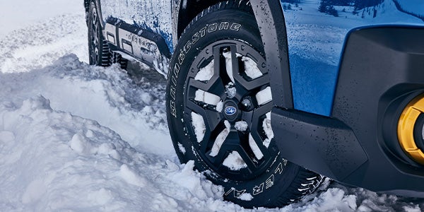 Close-up of a blue Subaru Outback Wilderness wheel in deep snow, showing the tire tread and black rim.