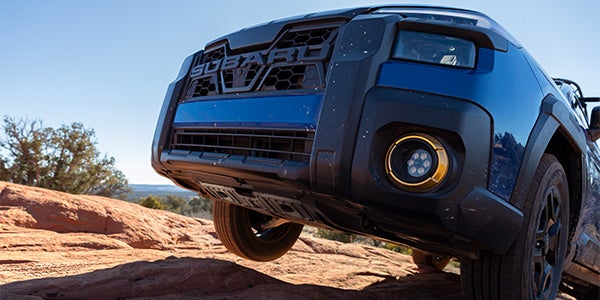 Front view of a blue Subaru Forester Wilderness off-roading on red rock terrain.