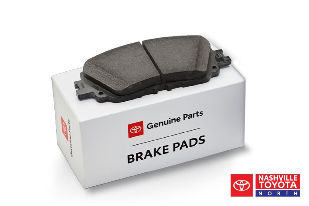 A pair of Toyota genuine brake pads sit on top of a white box labeled "Genuine Parts BRAKE PADS".