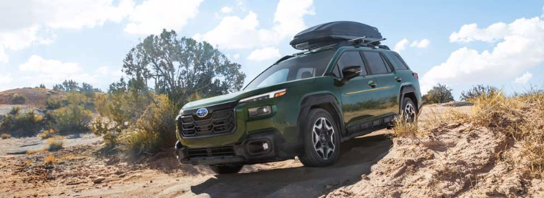 Front 3/4 action major of the 2026 Outback Touring in Deep Emerald Green Metallic with Thule roof cargo box accessory descending a bumpy dirt road in the desert.
