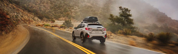 Rear 7/8 driver's side beauty action shot captured on windy road. Thule roof cargo box accessory on roof racks.