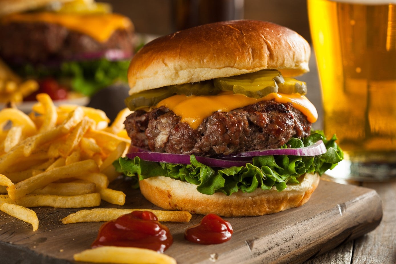 A cheeseburger on a wooden board, with ketchup and french fries.