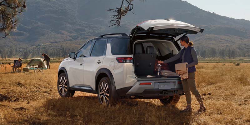 A person retrieving a lantern from the back of a white Nissan Pathfinder parked in the wilderness.