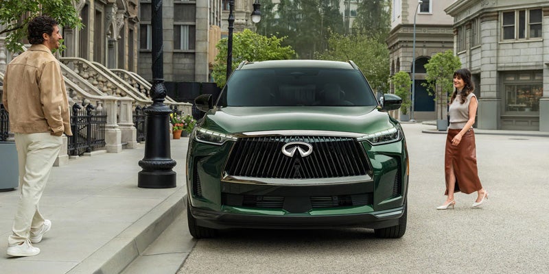A dark green Infiniti QX60 SUV parked on a city street, with a man and woman nearby.