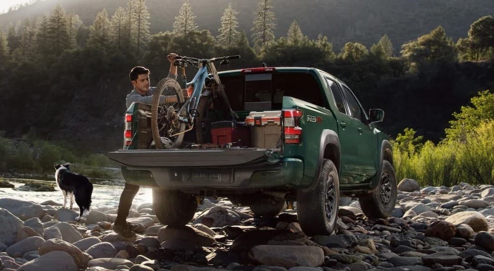 A person removing a bike from the bed of green 2026 Nissan Frontier Pro-4X.