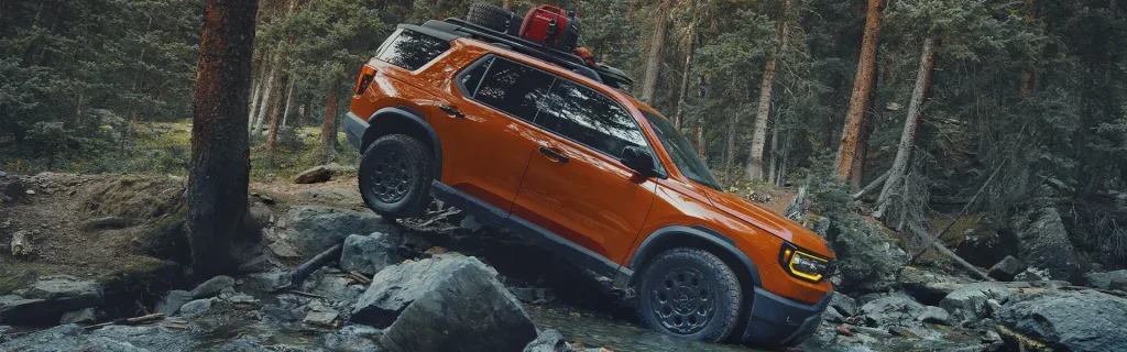 A rugged orange SUV navigating through rocky terrain in a forested area.
