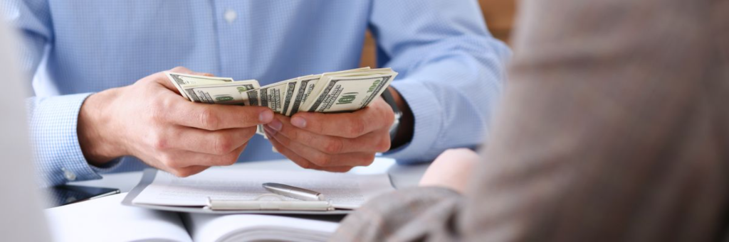 A person holding several hundred-dollar bills in their hands during a discussion.