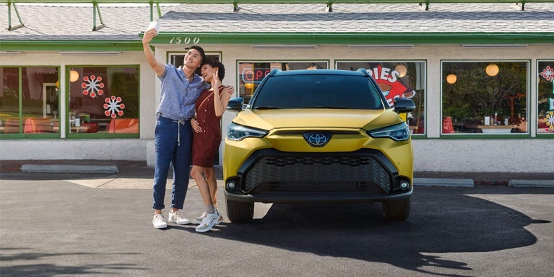 A yellow 2024 Toyota Corolla Cross and owners taking a selfie in front.