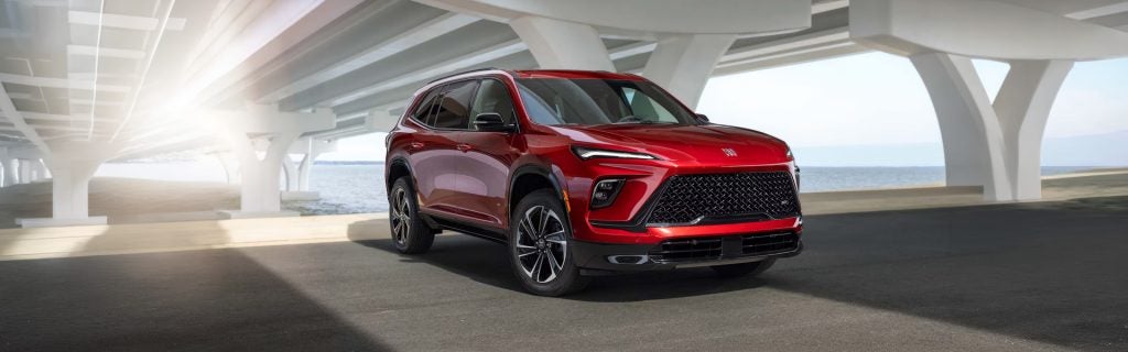 Red 2026 Buick Enclave SUV parked under a bridge near the water.