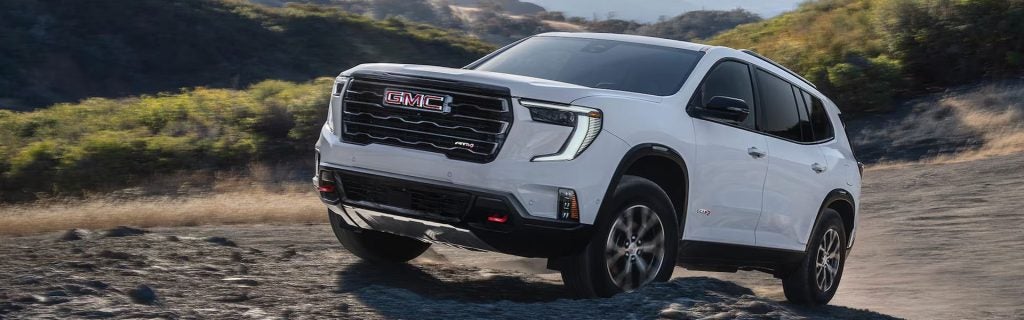 White GMC SUV driving off-road on a rocky trail in a rugged hillside landscape.