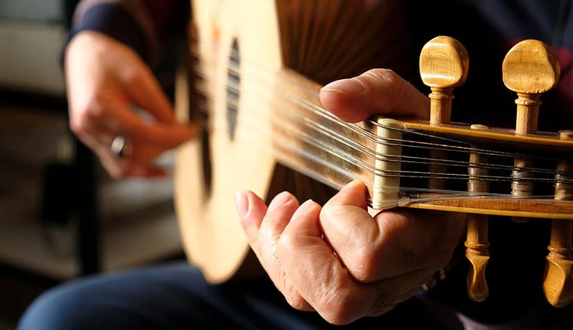 a close up shot of a mans hands as he plays an acoustic guitar 