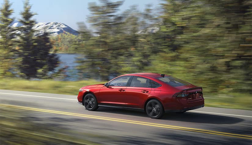 a red honda speeds along a road with trees and mountains in the background