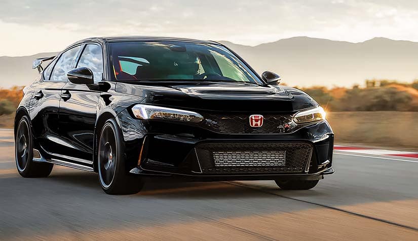 a black civic type r hatchback drives on a road with mountains in the background 