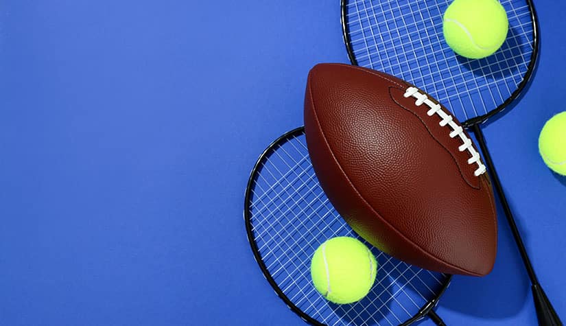 a football lays on two tennis rackets with three tennis balls 