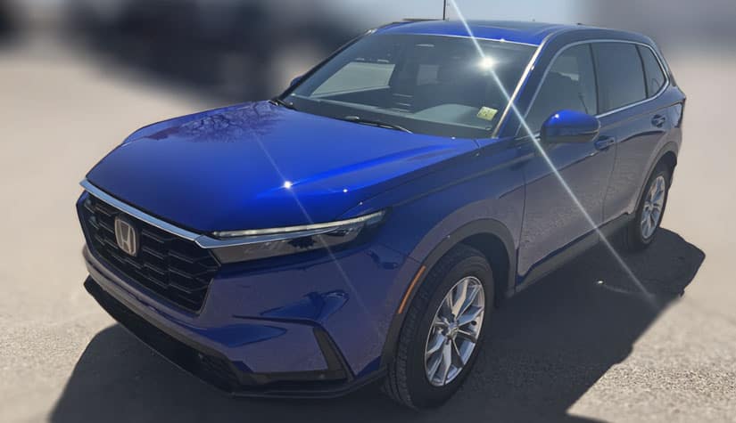 A blue honda sits on asphalt and the background has been blurred out 