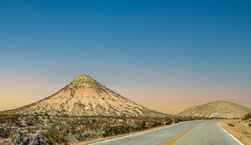 yellow sandy hills dotted with greenery against a blue sky turning to sunset 