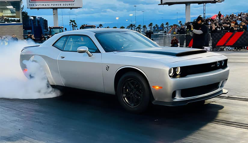 a silver challenger speeds over a finish line while a camera man records 