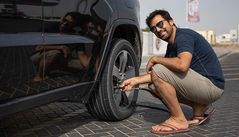 a man in flipflops smiles at the camera while filling up his tires with air 