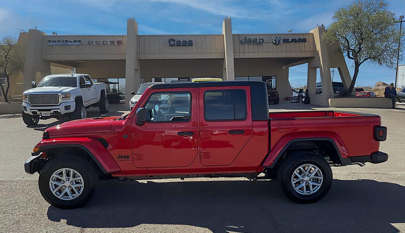 a red jeep truck sits in front of the casa dealership 