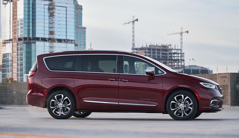 a burgundy chrysler pacifica minivan parked on a rooftop with modern glass buildings in the background 