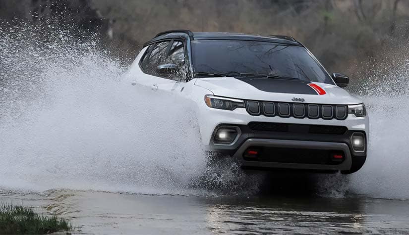 a white jeep compass drives through water and causes a big splash 