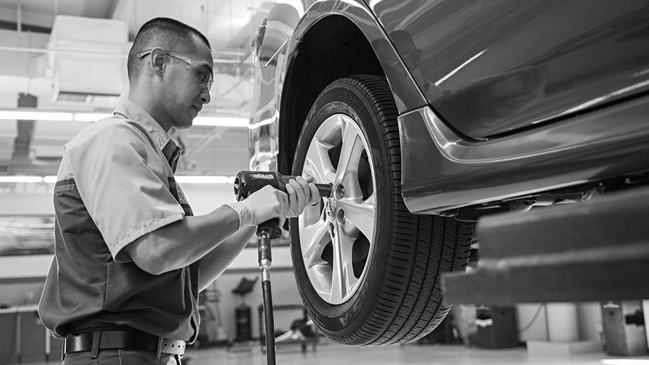 Grayscale image of a mechanic using an impact wrench to change a car tire on a lift.