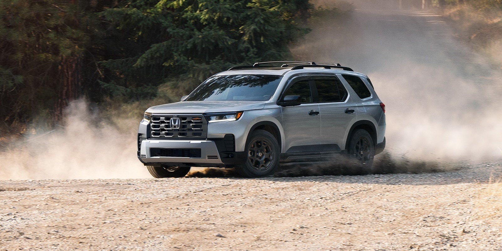 Silver Honda Pilot TrailSport kicking up dust on a dirt road.