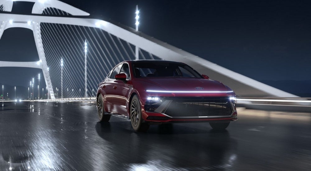A dark red 2025 Hyundai Sonata Limited Hybrid driving over an illuminated bridge at night.