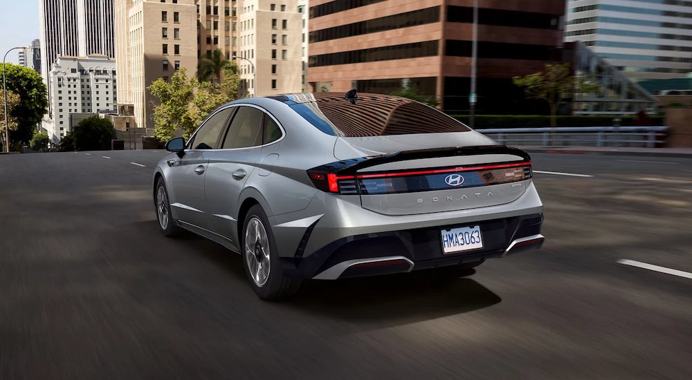 Rear view of a silver 2024 Hyundai Sonata Limited Hybrid driving on a city street.