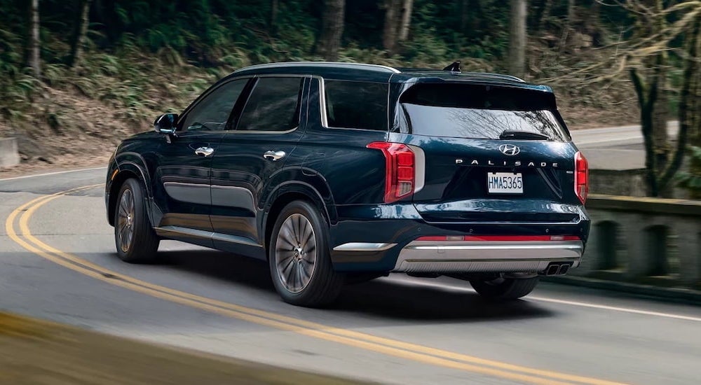 Rear of a blue 2026 Hyundai Palisade driving around a bend from a Hyundai Dealer Near Sevierville.