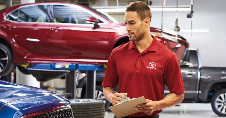 Toyota tech walking around a Toyota with a clipboard