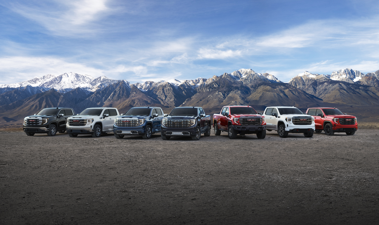 Lineup of seven GMC Sierra 1500 pickup trucks parked before snowy mountains