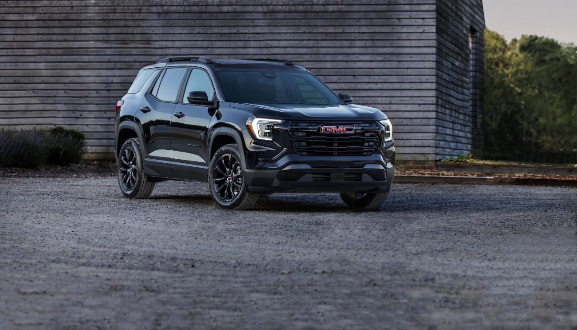 Black GMC Terrain Elevation parked on gravel beside a wood-clad barn