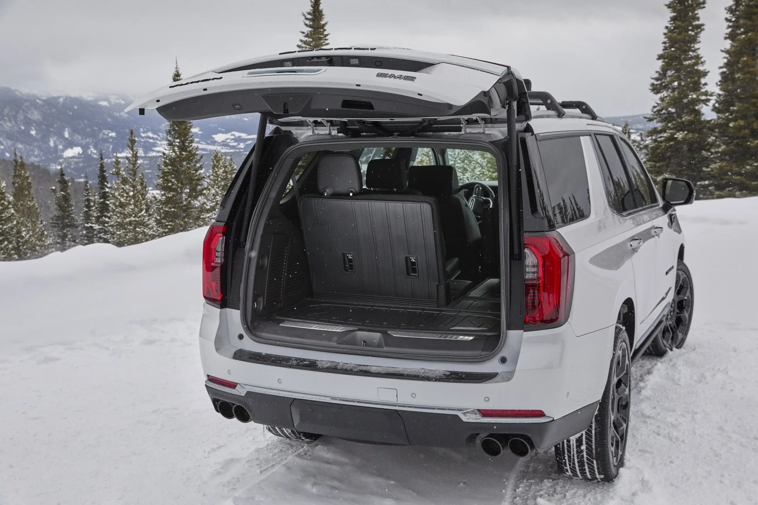 White GMC Yukon with liftgate raised, showing open rear cargo area in snow
