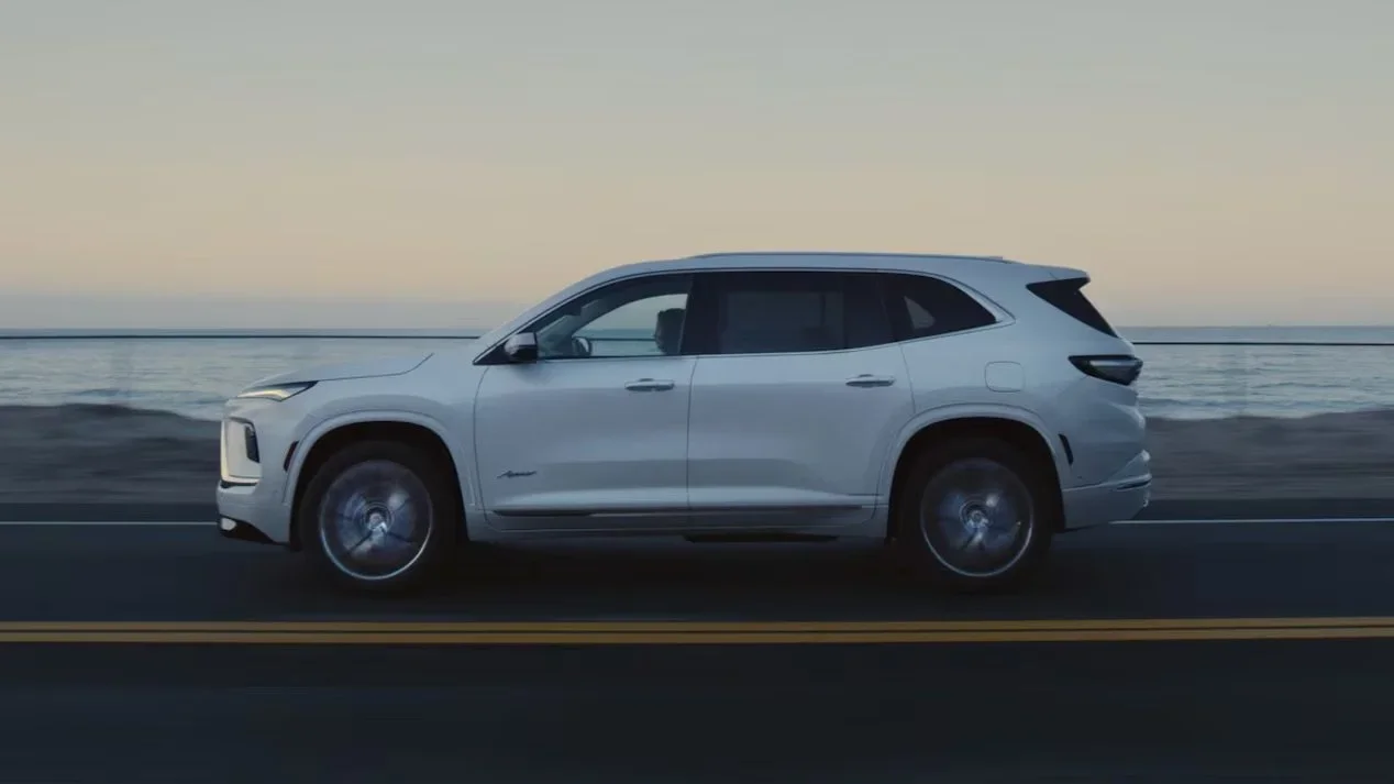 White Buick Enclave shown in profile driving a coastal road at dusk