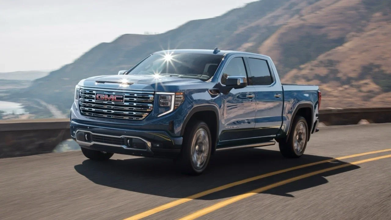Blue GMC Sierra 1500 Denali crew cab driving on a winding coastal highway