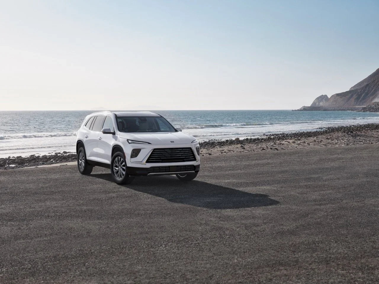 White Buick SUV parked on pavement beside a rocky ocean shoreline