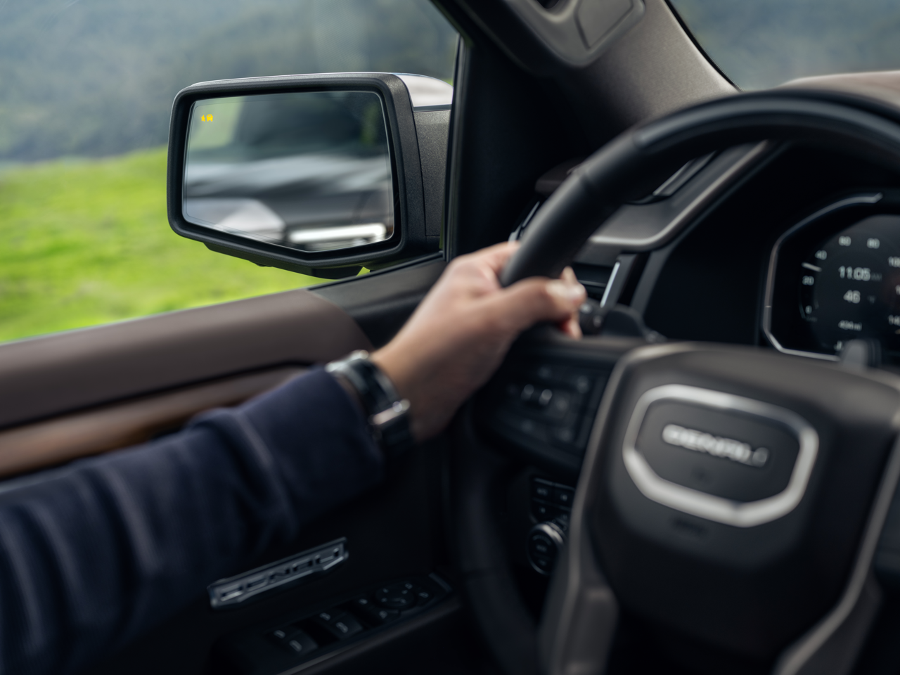 Driver's hand on GMC Sierra Denali steering wheel with blind spot alert in mirror