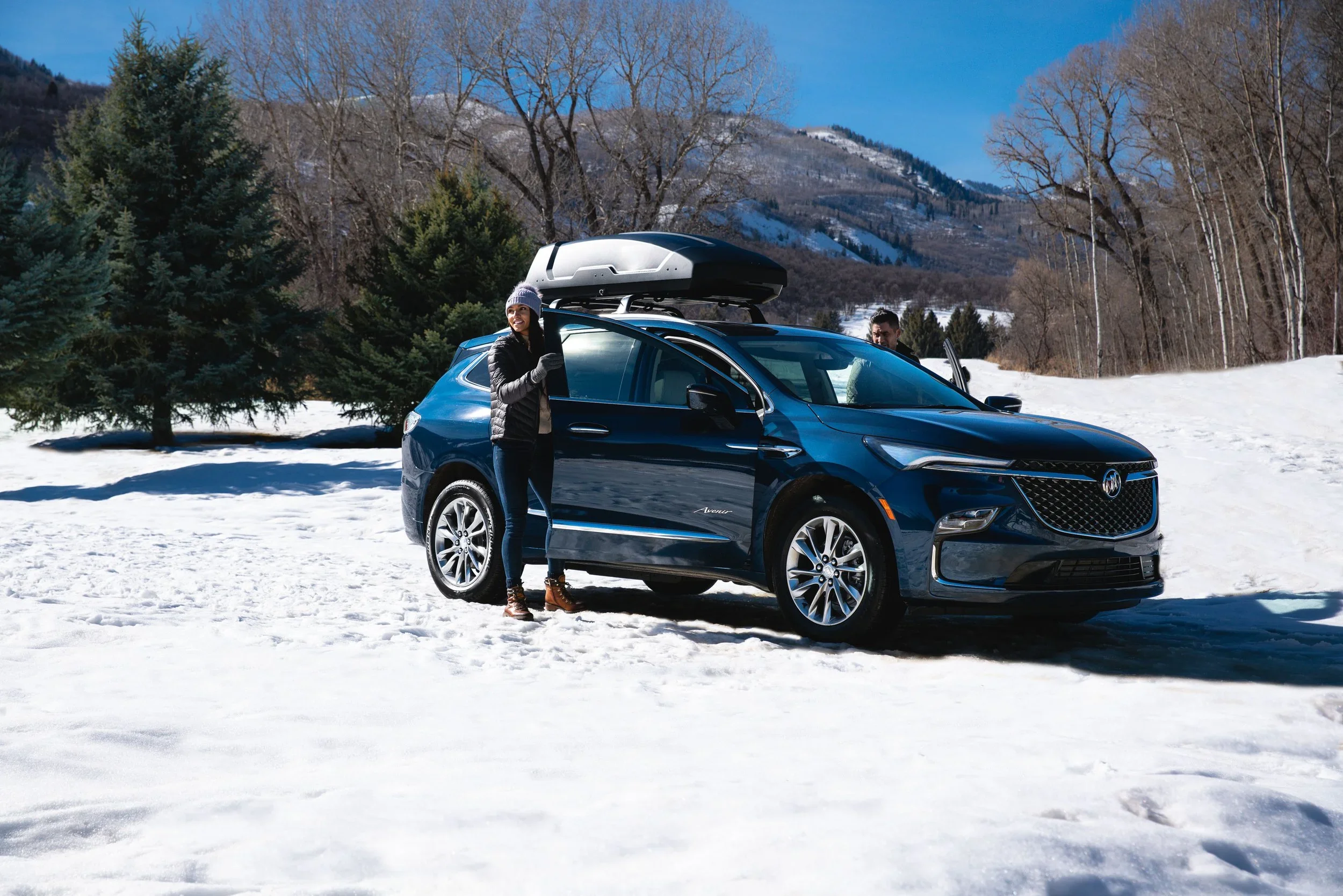 Blue Buick Enclave Avenir with roof cargo box parked in snowy mountain clearing