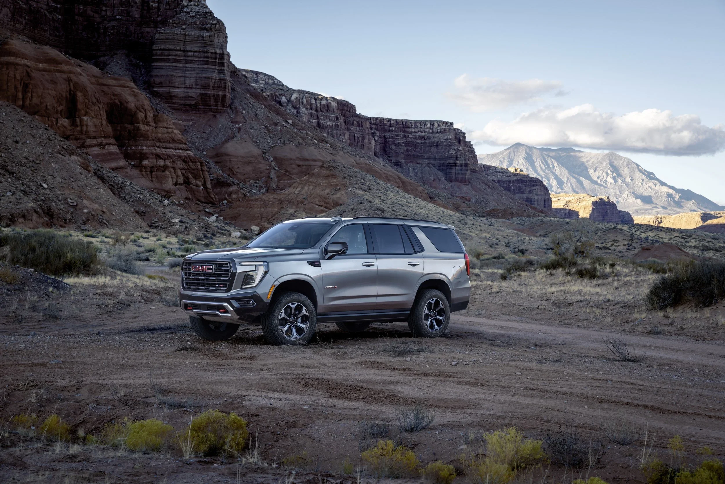 GMC Yukon AT4 parked on a desert dirt road below red rock cliffs