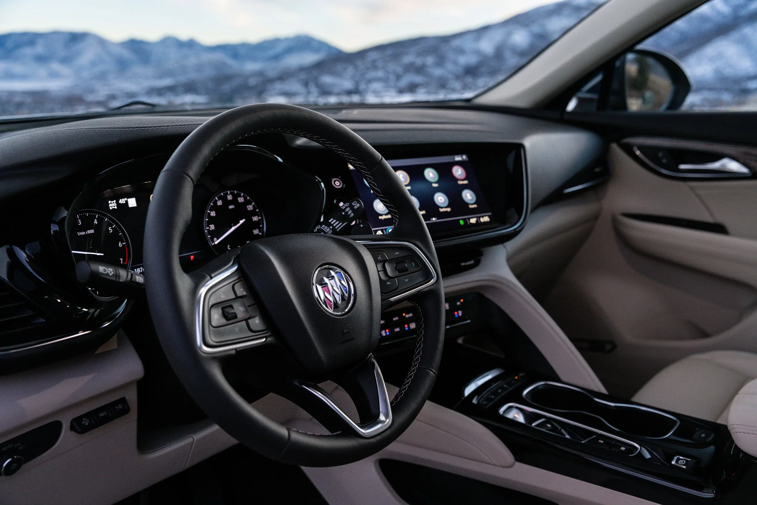 Buick Envision interior showing steering wheel, gauge cluster, touchscreen, and snowy mountains outside