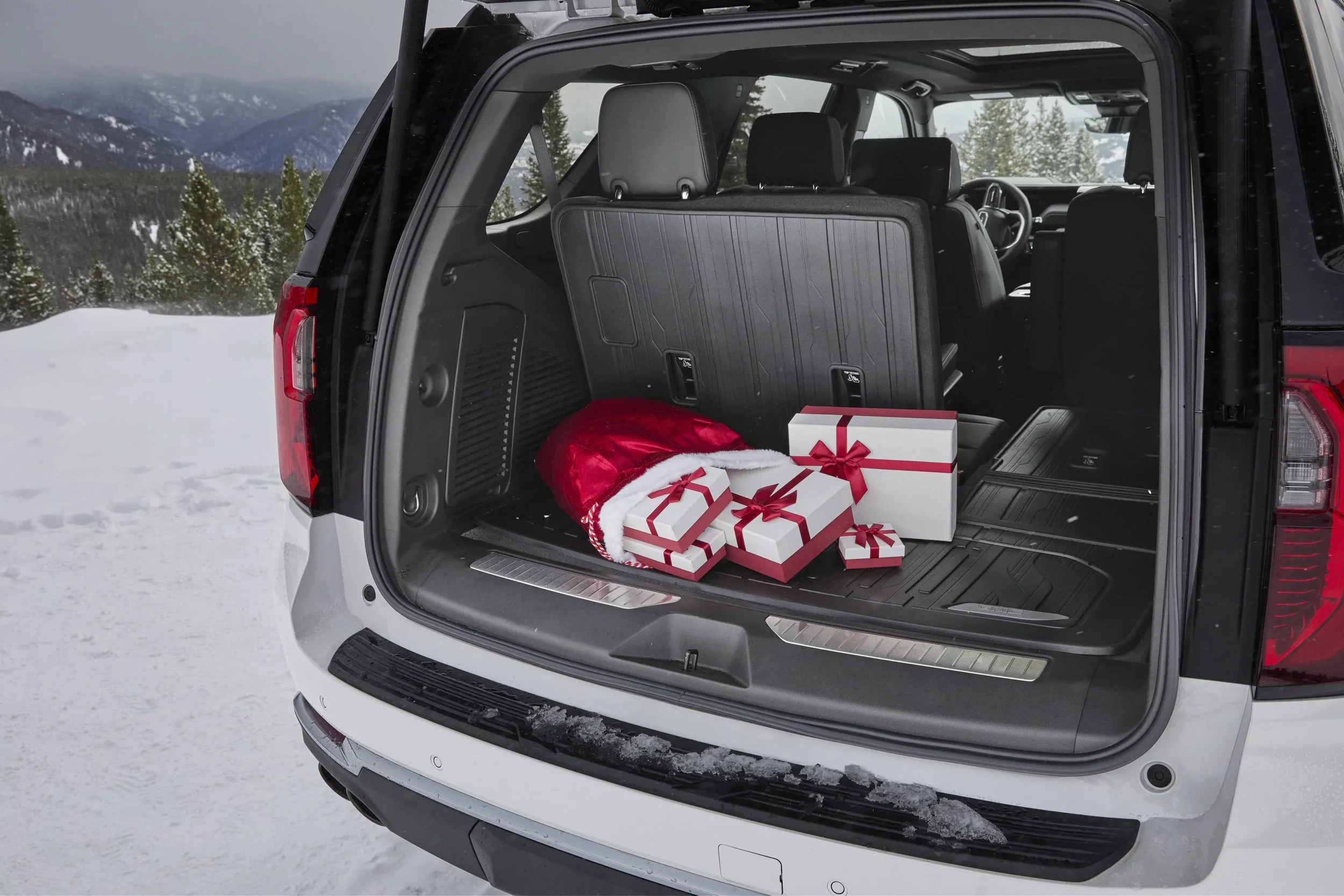 GMC Yukon open rear cargo area holding wrapped gifts in snowy mountains